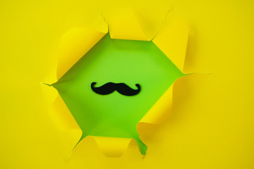ripped yellow paper against a green background with mustache in it.