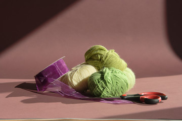 Woolen thread of green shades in balls with a purple ribbon and scissors