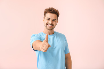Portrait of happy young man showing thumb-up gesture on color background