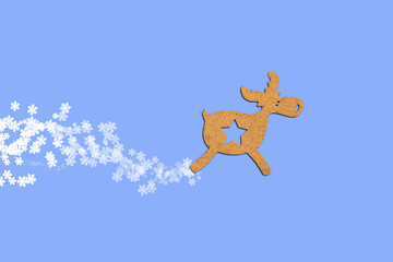 Wooden Christmas toy Deer with flying snowflakes from under the hooves on a blue background. Merry Christmas and Happy New Year concept. Minimalistic style. Flat lay, top view