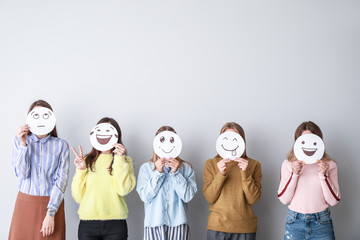 Group of woman covering their faces with drawn emoticons against light background