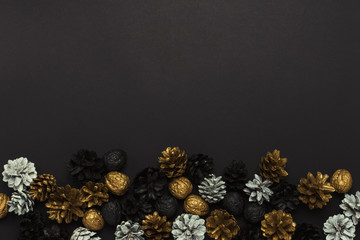Obraz na płótnie Canvas Pine cones and nuts painted in golden, black, white colors on a black background. Concept of Happy New Year and Merry Christmas. Flat lay, top view