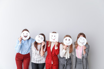 Group of woman covering their faces with drawn emoticons against light background