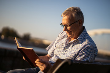 Outdoor portrait of senior man who is reading book.