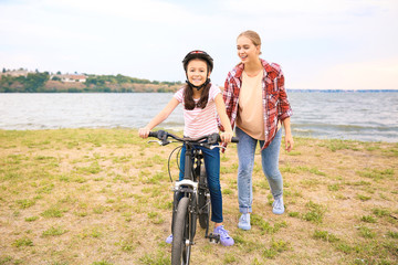 Mother teaching her daughter to ride bicycle outdoors