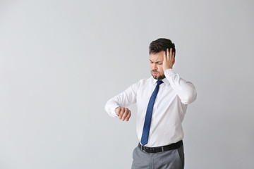 Portrait of troubled businessman looking at watch against light background