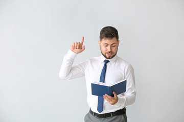 Portrait of handsome businessman with book and raised index finger on light background