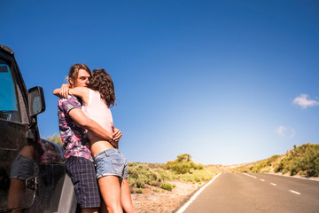 Coloured style caucasian young beautiful couple standing and hugging outside a black car during alternative travel vacation. together - concept of youthful and wanderlust for alternatie people