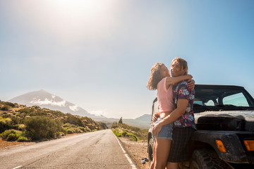 Sunny style caucasian young beautiful couple standing and hugging outside a black car during alternative travel vacation. together - concept of youthful and wanderlust for alternatie people