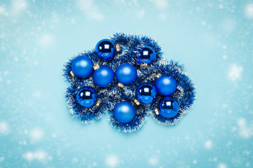 Blue Christmas tree toys, balls on a blue background with falling snow. Concept of Merry Christmas and Happy New Year. Flat lay, top view