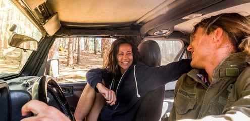 Couple of young friends sit down inside the car together having fun and enjoying the travel - forest outdoor in background -concept of relationship for cute people