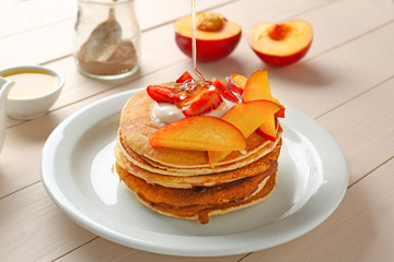 Pouring of honey onto tasty pancakes on table