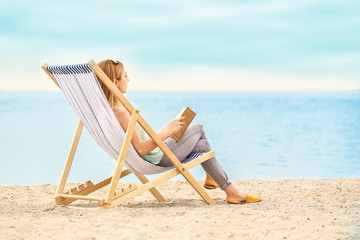 Woman reading book while relaxing on sea beach