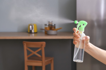 Woman spraying air freshener in kitchen