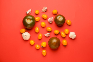 Different fresh tomatoes and garlic on color background