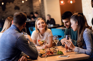 Group of young friends having fun in restaurant, talking and laughing while dining at table.