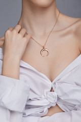 Cropped shot of a lady, wearing white chest tied shirt. She has golden necklace with suspension in...