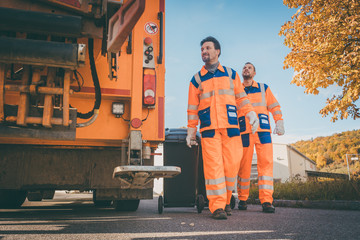 Two refuse collection workers loading garbage into waste truck