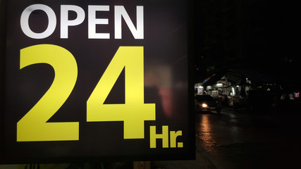 Open 24 hours label (tag),sign on the road side at night with blurred background of moving car. This is symbol of advertising for service everyday, every time, all day and all night. business concept