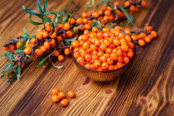 orange glass bowl with sea buckthorn berries and branches on wooden background