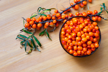 glass bowl with berries and sea buckthorn branches on wooden background top view