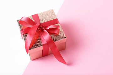 Gold color gift box with pink ribbon on pink background close-up, copy space.