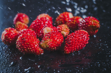 Bright red wild strawberries on a black background in the water.