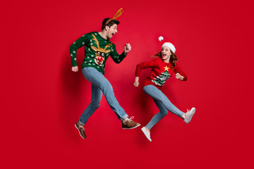 Fototapeta na wymiar Full body photo of excited jumping couple rushing for x-mas discounts wear ugly ornament jumpers isolated red color background