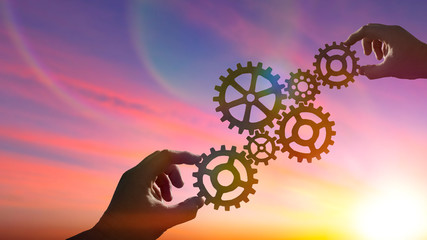 Hands of businessmen connect gears to puzzle on sunset background. Concept business ideas,...