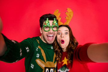 Obraz premium Photo of excited lady and guy chilling at x-mas costume party making selfies wear funky pullovers with ugly ornaments isolated red color background