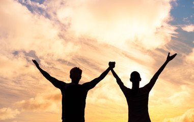 Silhouette of man and woman together with hands raised. Happy couple outdoors. 