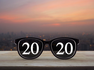 2020 white text with black eye glasses on wooden table over blur of cityscape on warm light...