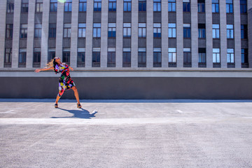 Beautiful woman in a colourful dress dancing and jumping on a rooftop.
