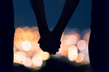 Couple holding hands facing city night lights. 