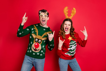 Portrait of two people wife husband with brown wavy hair scream have theme rock-and-roll show horn sign wear funny eywear seasonal christmas tree pullover denim isolated over red color background