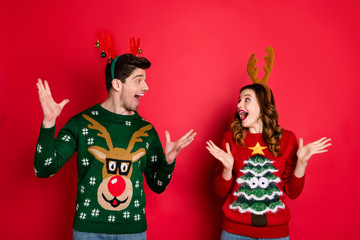 Portrait of amazed two masquerade people wife husband with brunet hair hear news scream wow wear seasonal christmas tree comfort sweater fashion decor jumper isolated over red color background