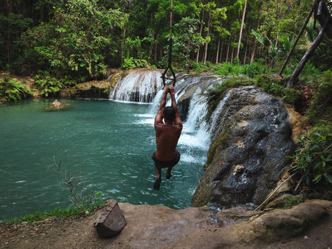 man swinging with the rope at the pool of waterfalls, Cambugahay Falls on Siquijor Island in Philippines
