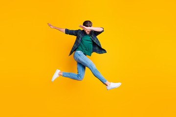 Fototapeta na wymiar Full body photo of cheerful content dream funky man jump have fun dance like true clubber enjoy summer vacation wear denim jeans sneakers checked green shirt isolated over yellow color background