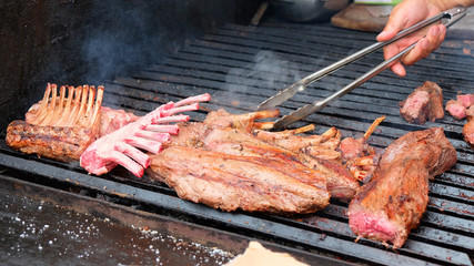  grilled pork ribs, food on the street, the hand of a man with tongs turns the pork ribs on the grill