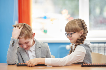 young schoolgirl with glasses helps a friend use abacus soroban