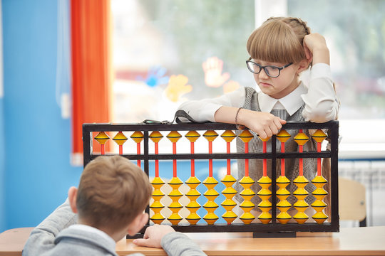 young schoolgirl with glasses helps a friend use abacus soroban