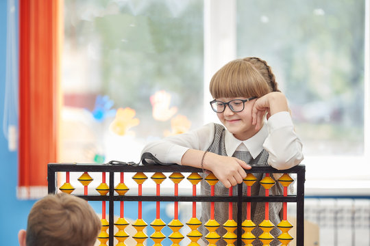 young schoolgirl with glasses helps a friend use abacus soroban