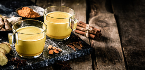 Turmeric golden milk and ingredients on wood background, copy space