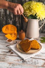 pumpkin and pumpkin cakes, honey stick held by male hand, runny honey, wooden background, autumn flowers, cinnamon in a little bowl