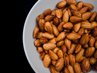 Closeup fresh almonds in white dish on dark table background, Fresh almonds are material for almonds milk.