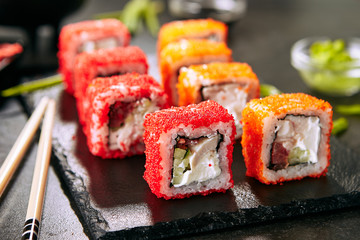 Macro shot of chicken maki sushi rolls with rice, cream cheese, chicken fillet, tomato, cucumber, red flying fish caviar and nori. Fresh tory teriyaki uramaki roll on black stone background closeup © Ryzhkov