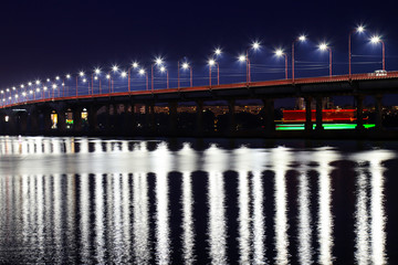 The night bridge with beautiful lanterns is reflected in the water on the Dnieper River, in the Dnepropetrovsk city, Ukraine. Evening river landscape in a big city.