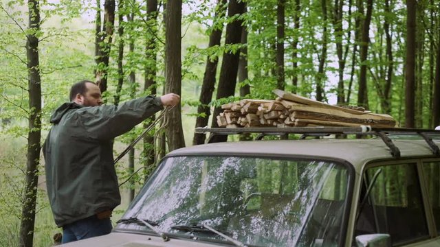 Slow Motion Of Casual Strong Man Works with Firewood and Rope near Car in Wild Deciduous Forest.