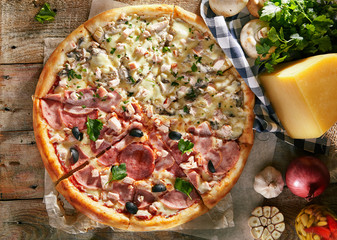 Pizza in half with chicken and mushrooms, on the other - ham and bacon with olives and fresh herbs on boards with vegetables