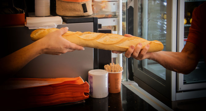 Commer&ccedil;ant boulanger artisan - cliente achetant une baguette de pain fra&icirc;che dans sa boulangerie en France
